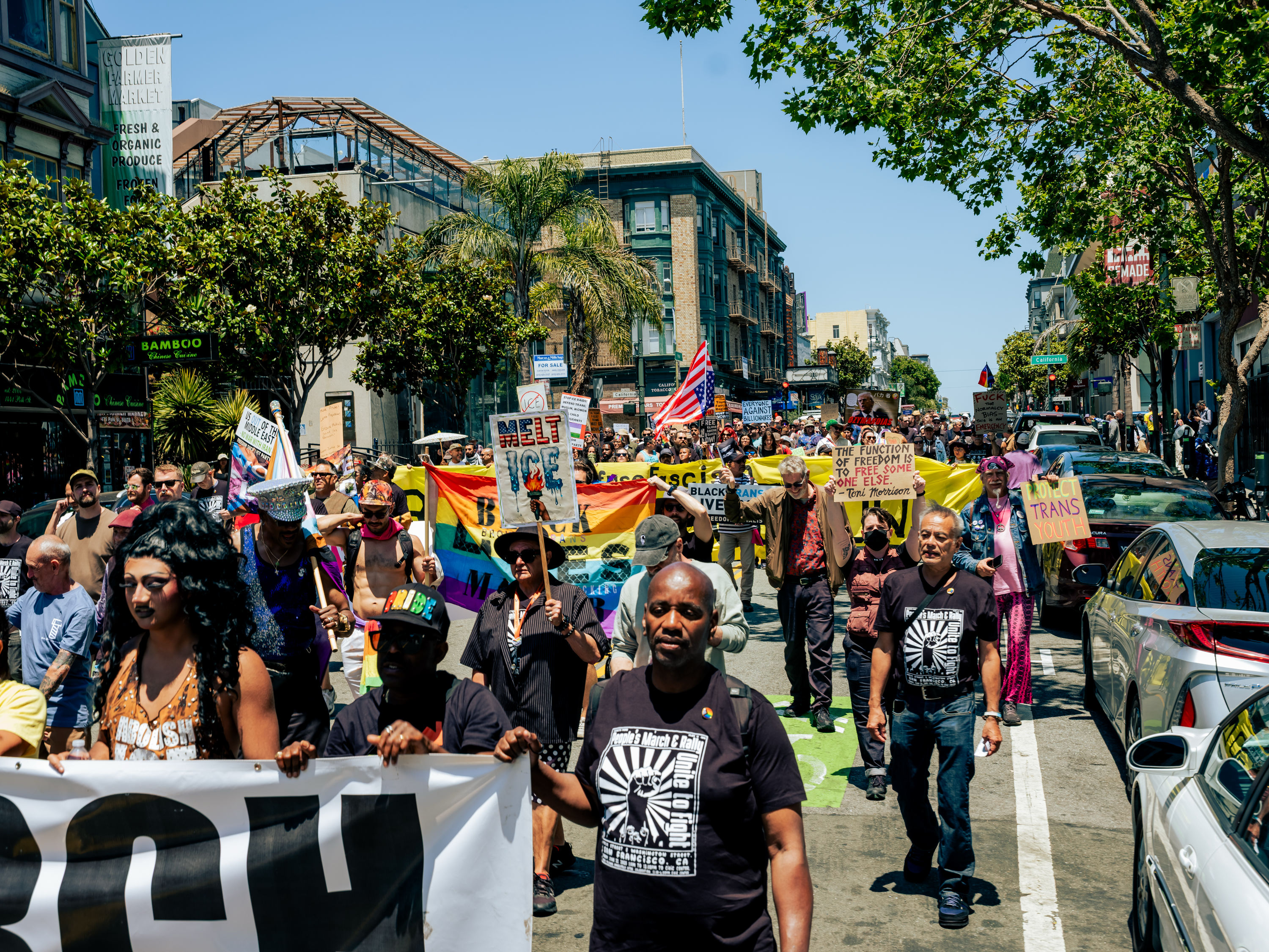 A diverse group of people is marching down a street, holding colorful signs and banners advocating for LGBTQ+ rights and social justice.