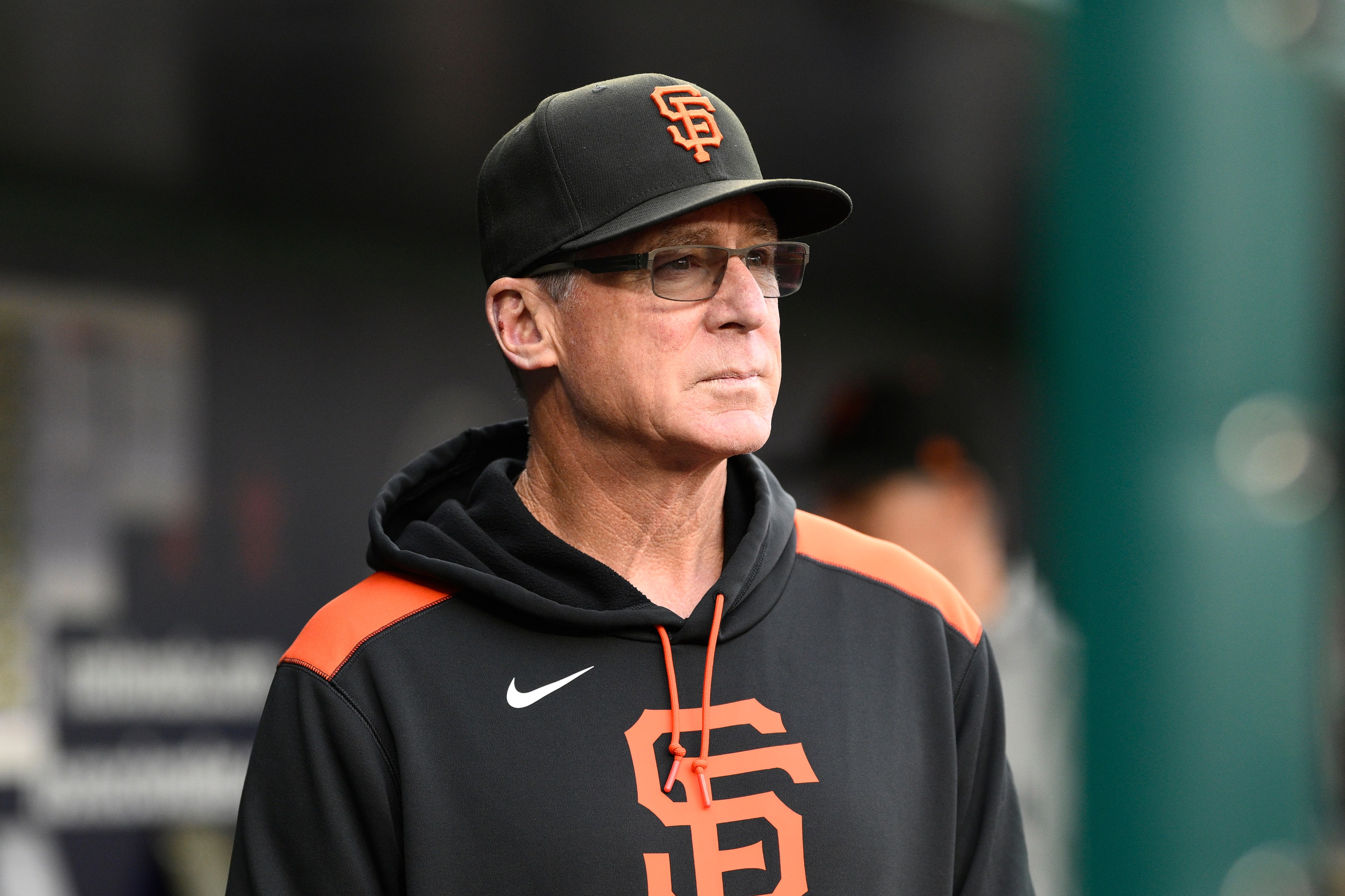 A man in a black hoodie and cap with an "SF" logo stands in focus, looking serious, with a blurred background.