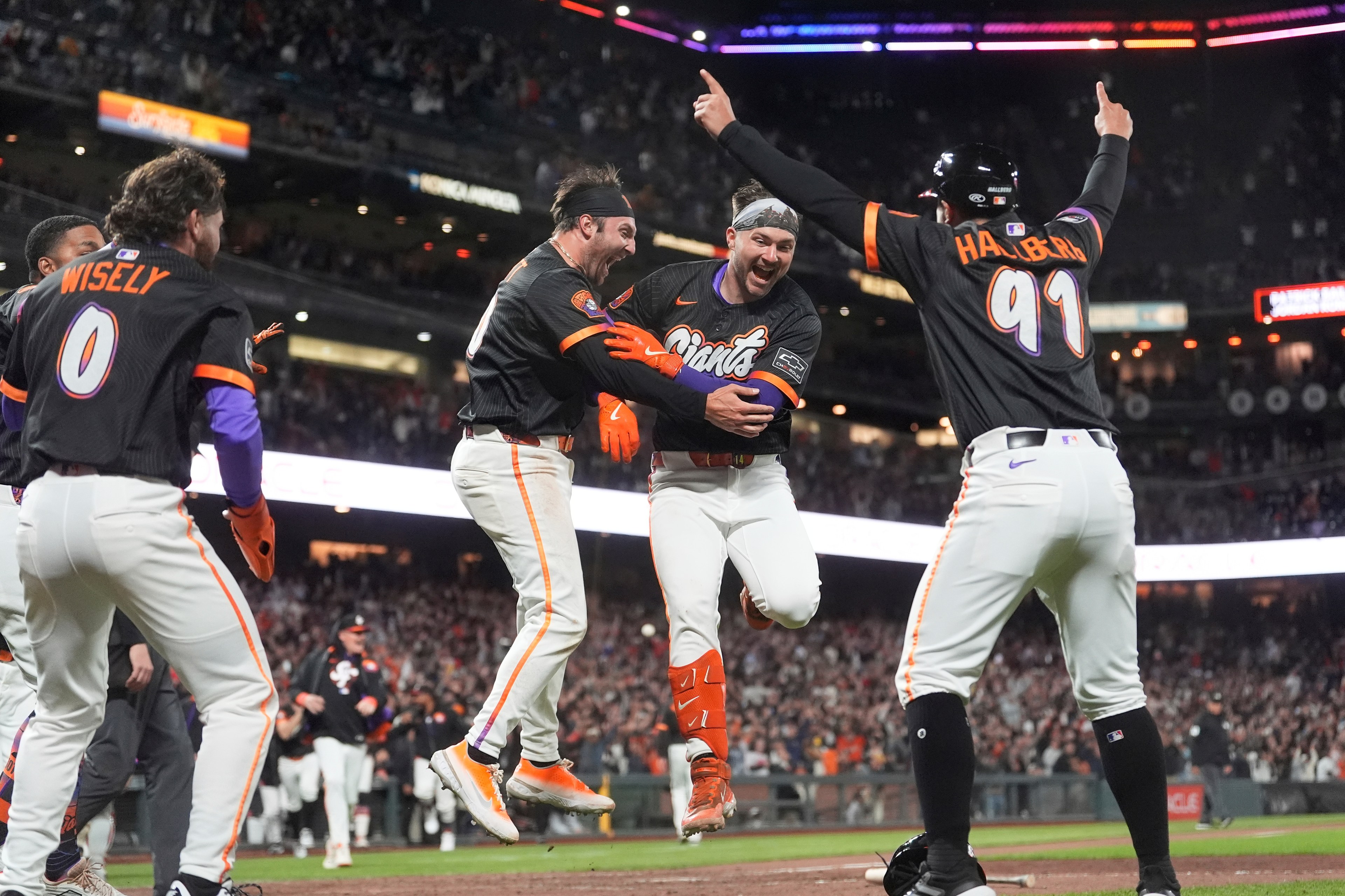 Baseball players in black uniforms joyfully celebrate on the field amid a cheering crowd, jumping and embracing each other.