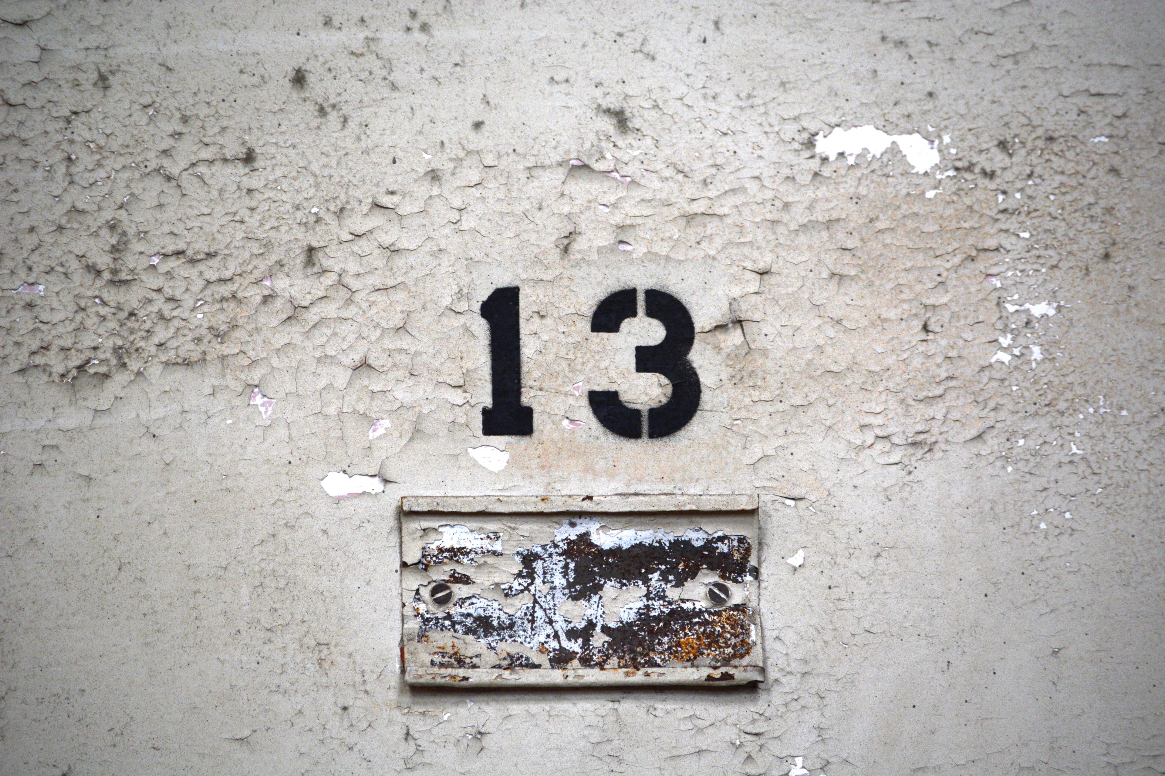 The image shows a weathered, peeling wall with the black number &quot;13&quot; stenciled above a rusted and worn metal plate.