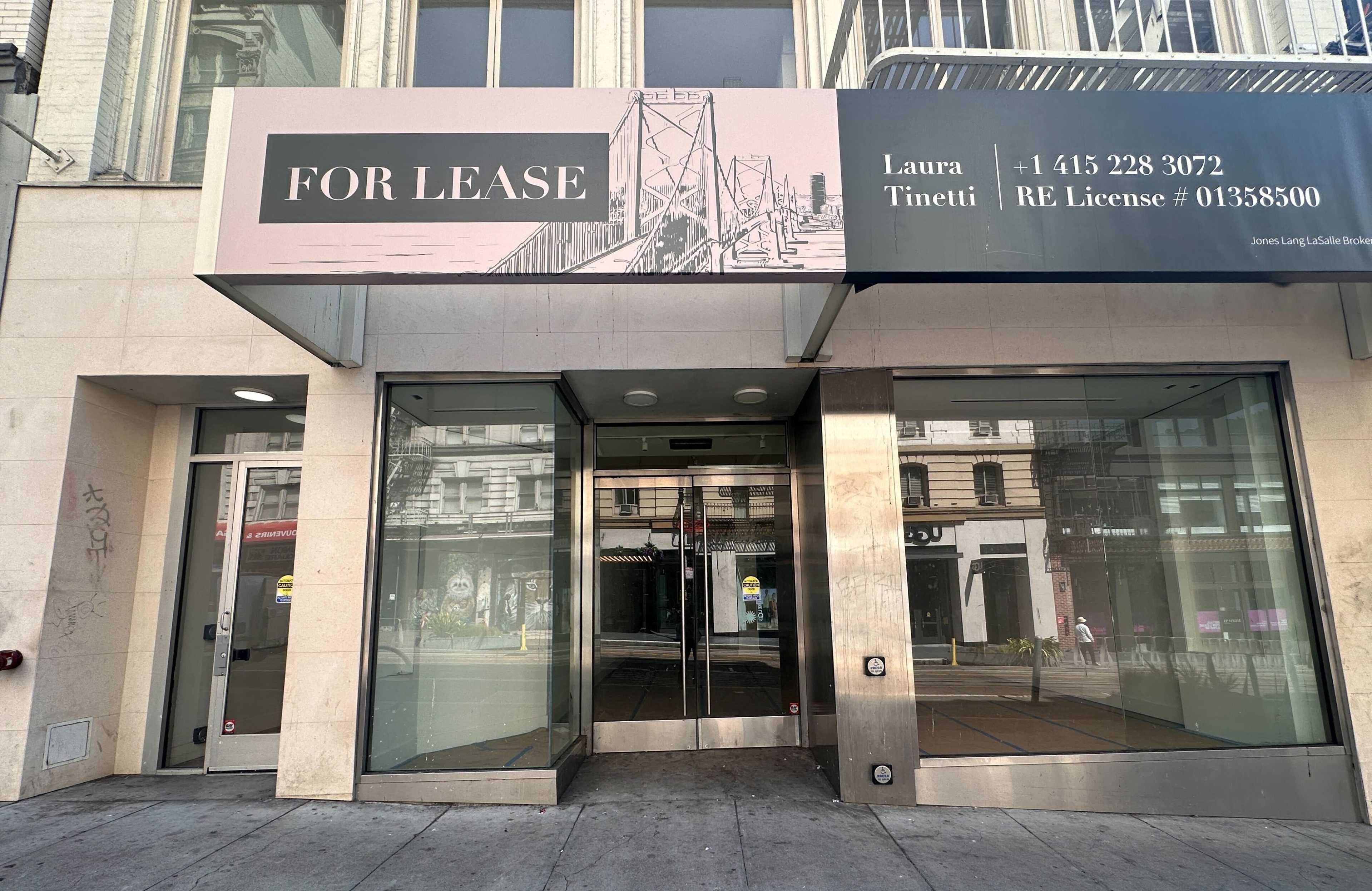 A commercial storefront with glass doors displays a &quot;For Lease&quot; sign. The contact information and a bridge illustration are above the entrance.